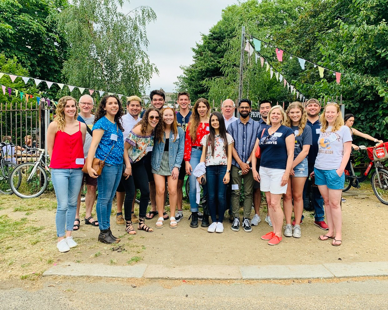 A group of UC students stand among UC alumni at an outdoor 4th of July barbecue in a London park.