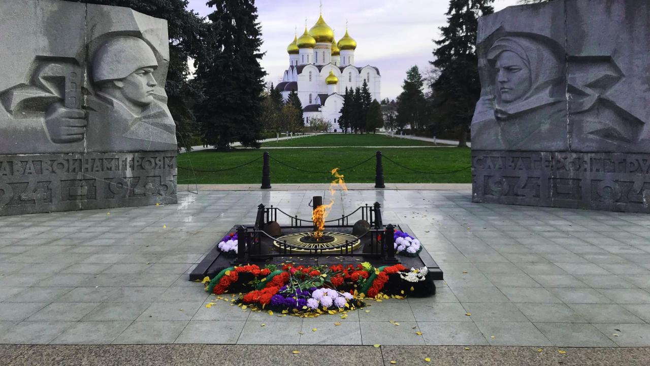 A stone memorial commemorating World War II, flowers and a flame sit at the center. In the background stands the white and gold Assumption Cathedral. (Courtesy of Cameron Lallana) Header Image, Article
