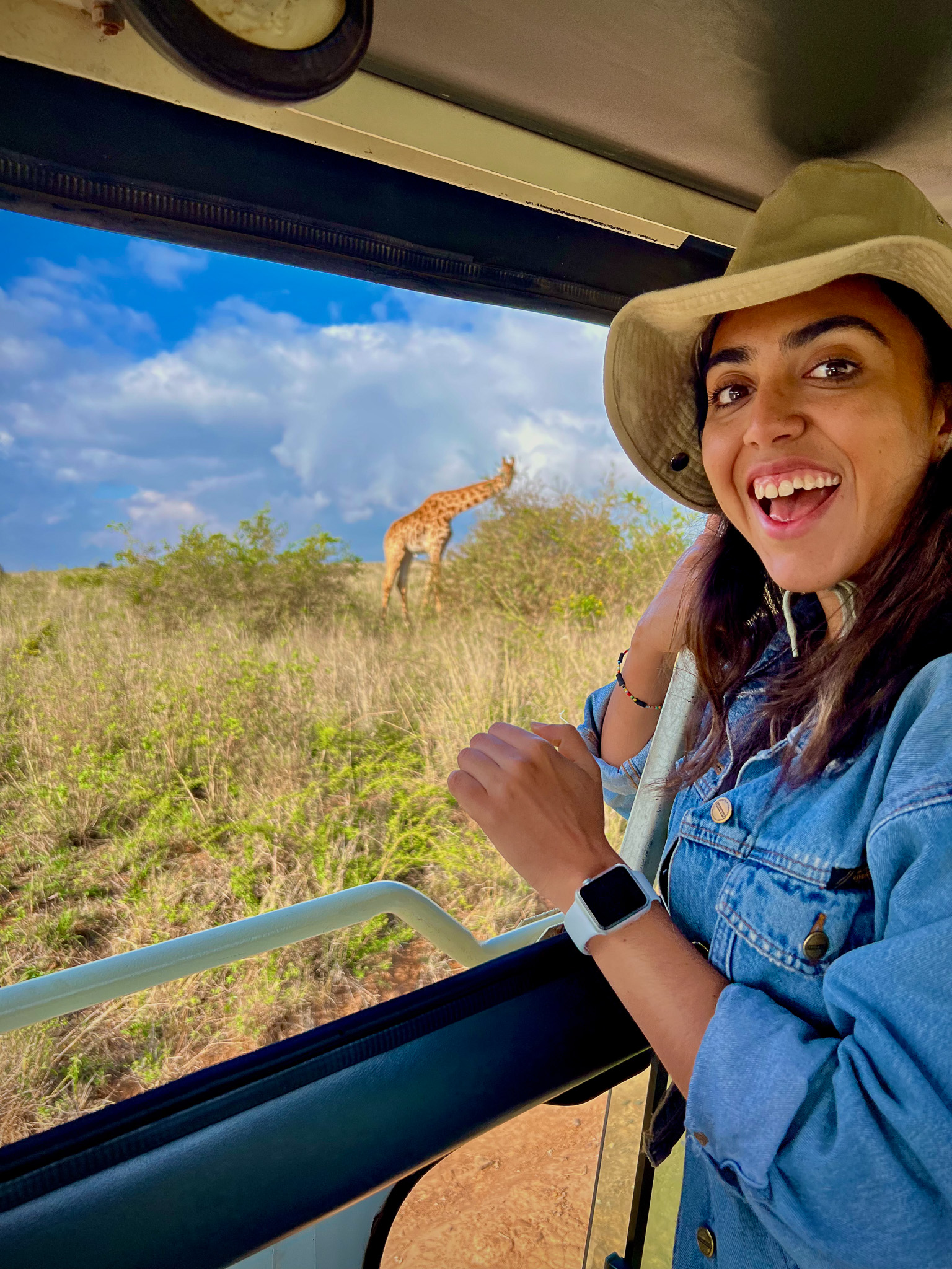 Student on a Safari in Kenya. She is smiling into the camera. A giraffe is off in the distance.