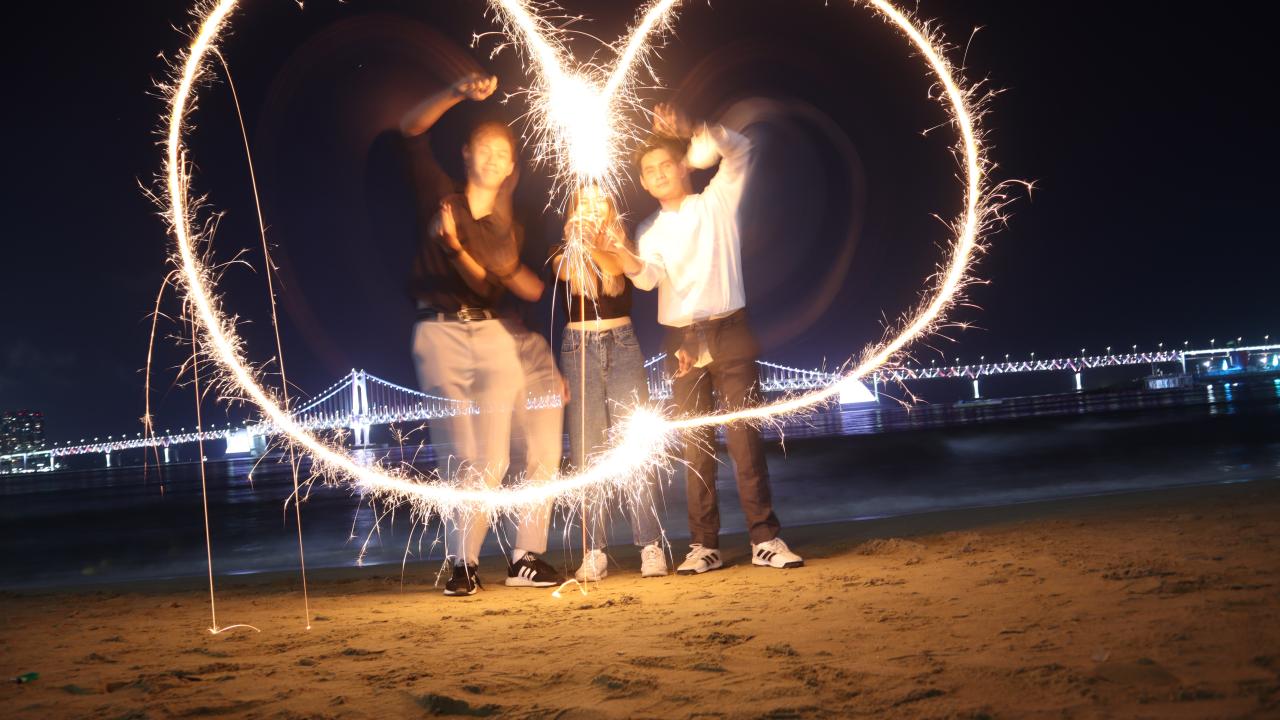 Students on a beach trying to use fireworks to make a heart shape.