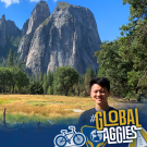 UC Davis international student, Rosh Ho, is standing in front of green and yellow grass in Yosemite National Park, with large mountains in the background.