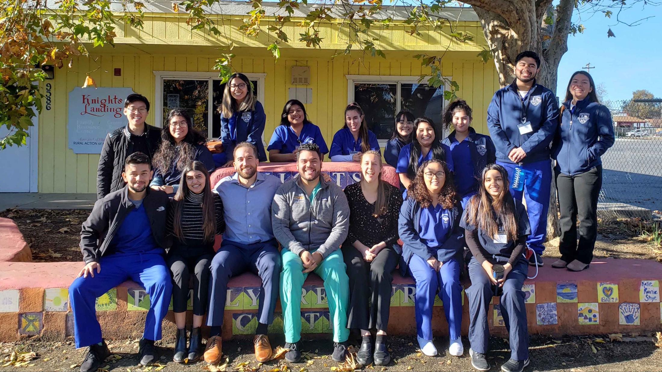 A group of about a dozen students posing for a photo in front of a community building in Knights Landing, CA