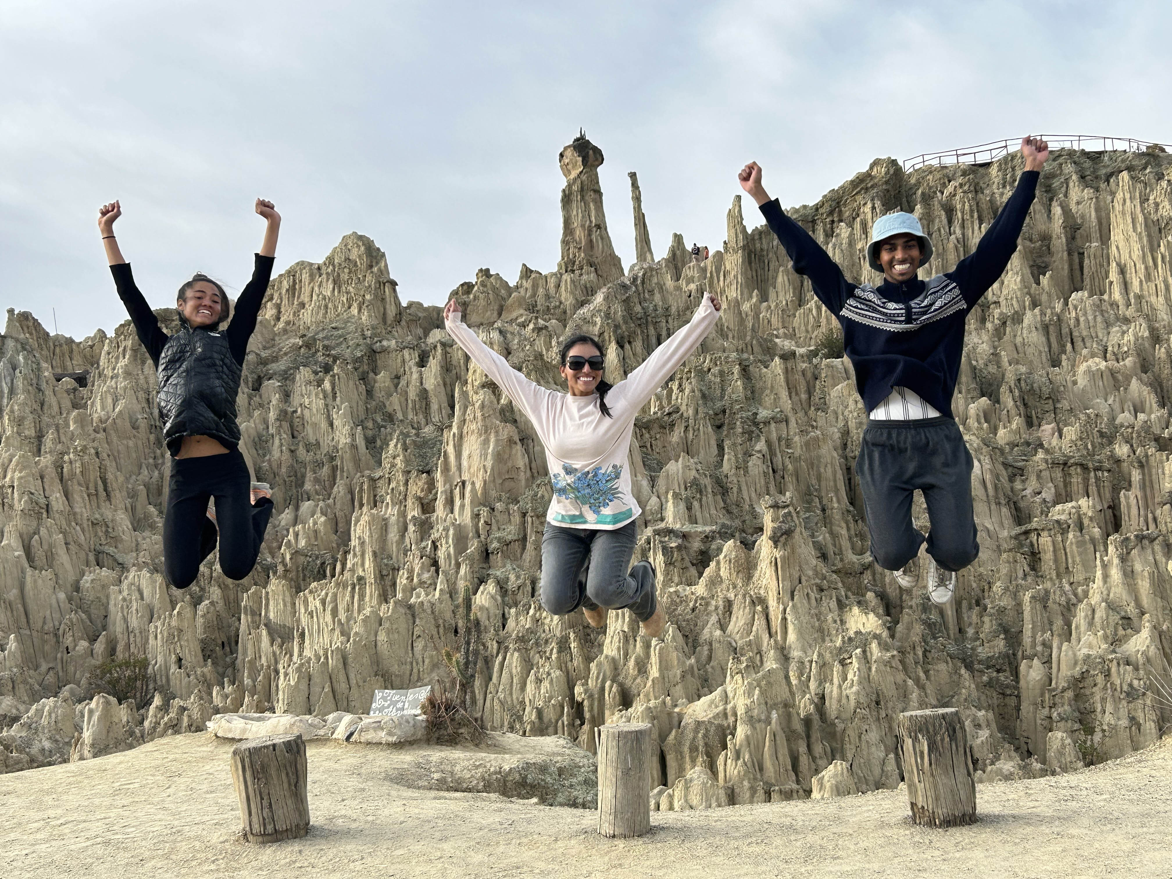 Three student in a large canyon. The all jump in the air at the same time and the photo captures them high in the air, smiling.