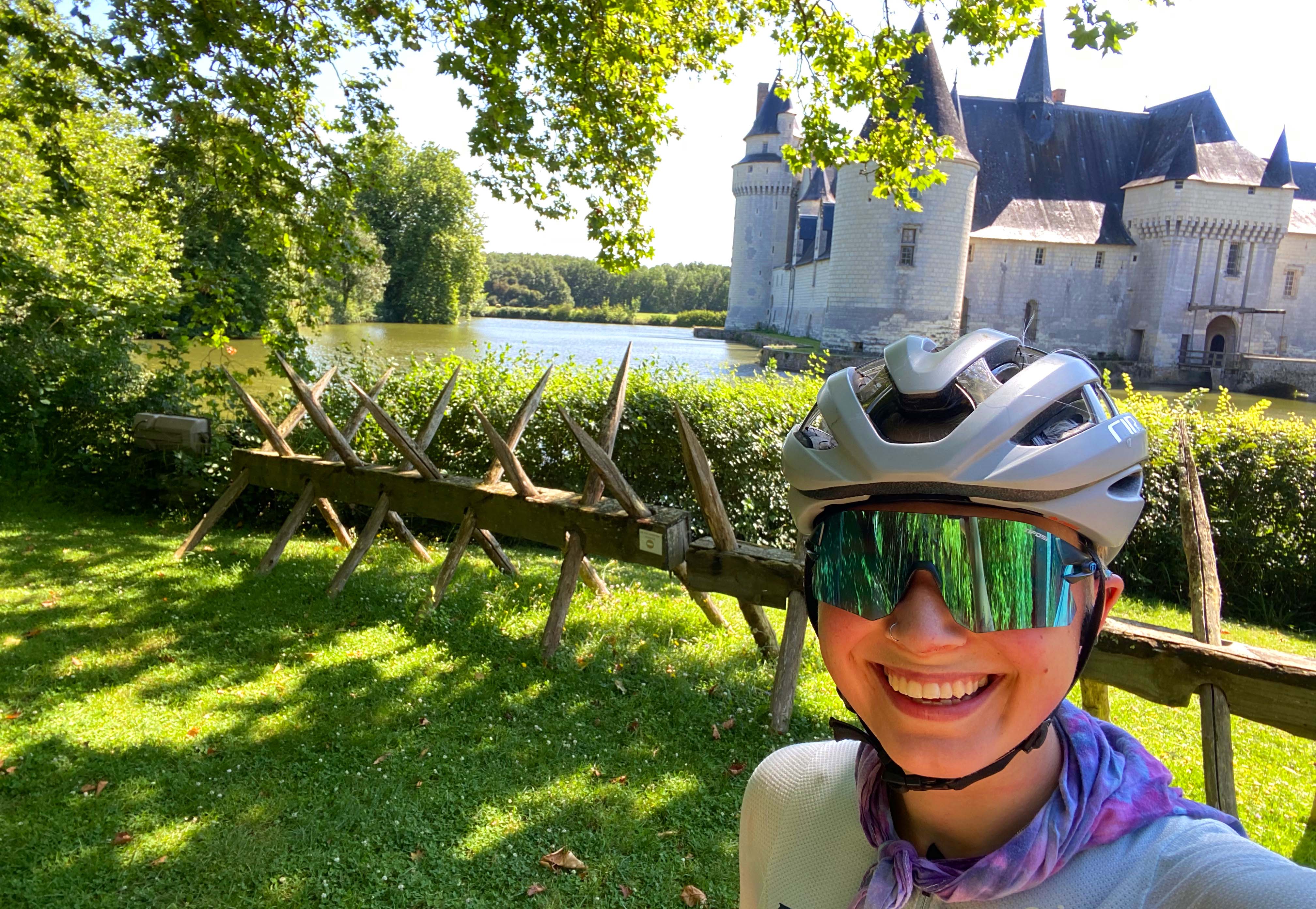 Person in cycling gear smiling with a chateau and moat in the background.