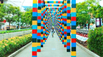 Image of a student riding a bike between a row of colorful pillars