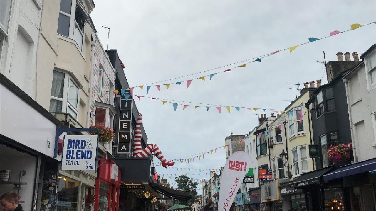 A street view of North Laine. Pink, blue, and yellow pennants blow in the wind. Blog Post, Header Image