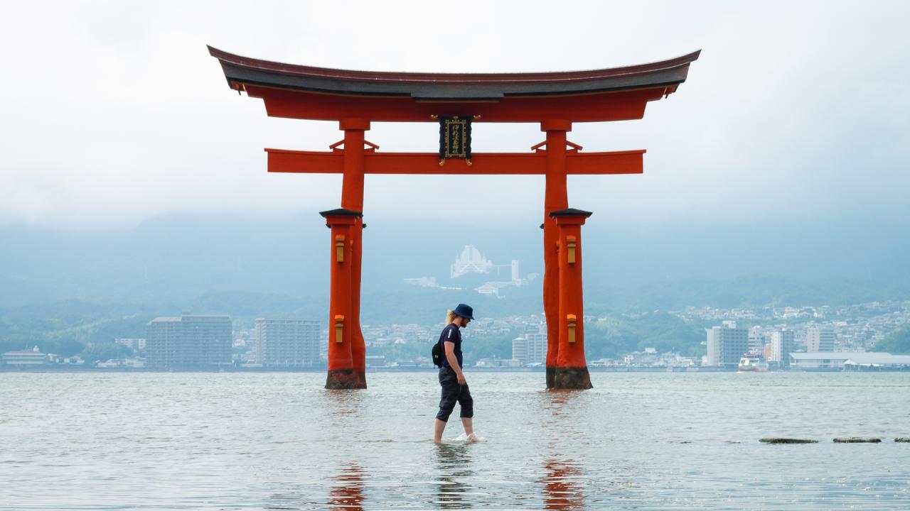A man stands in calm water, reflecting the serene surroundings and the clear sky above.