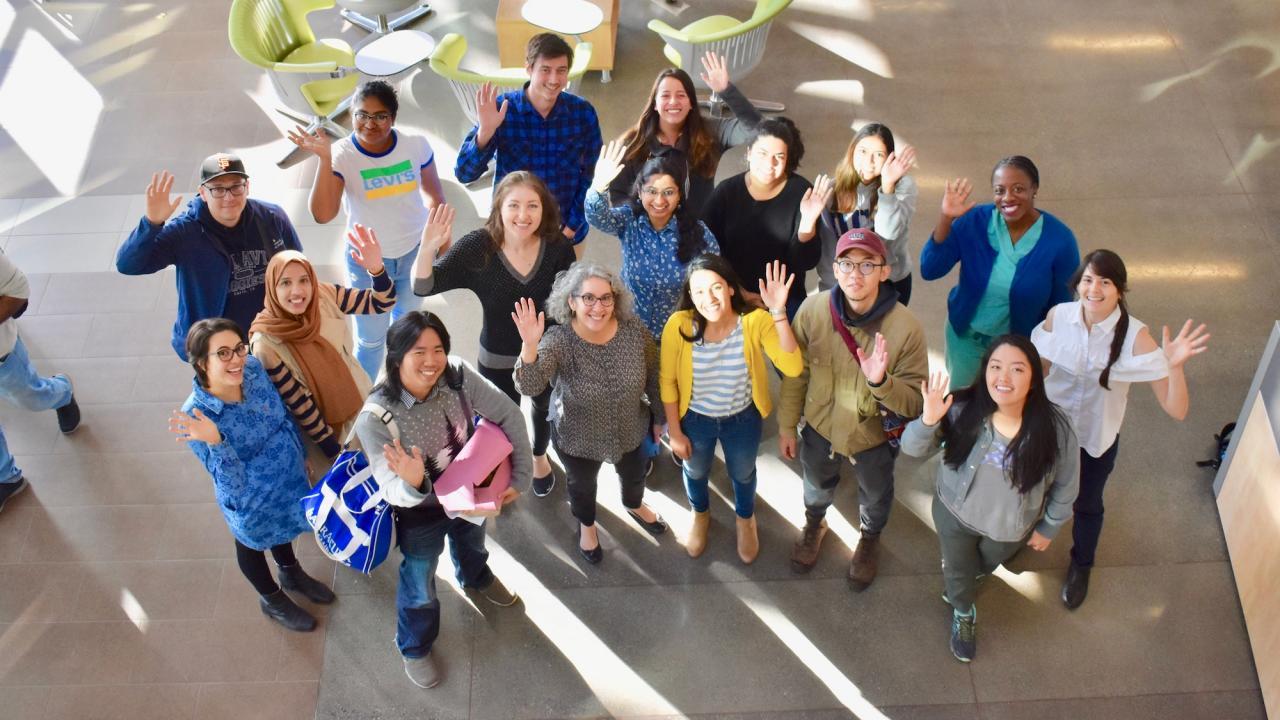 A group of students and staff looking up towards the camera, smiling and waving
