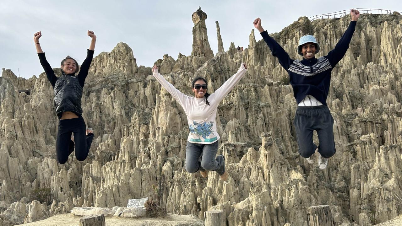 Three student in a large canyon. The all jump in the air at the same time and the photo captures them high in the air, smiling.