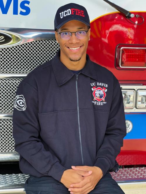 Comeaux seated on a fire truck with a blue UC Davis fire department jacket and hat.