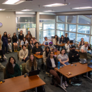 Students sit at their desks smiling for the camera