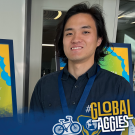 Photo of a student standing on front of a poster board. He is smiling. There is also a Global Learning Hub logo in the bottom left corner and a Global Aggies graphic/logo in the bottom right corner 