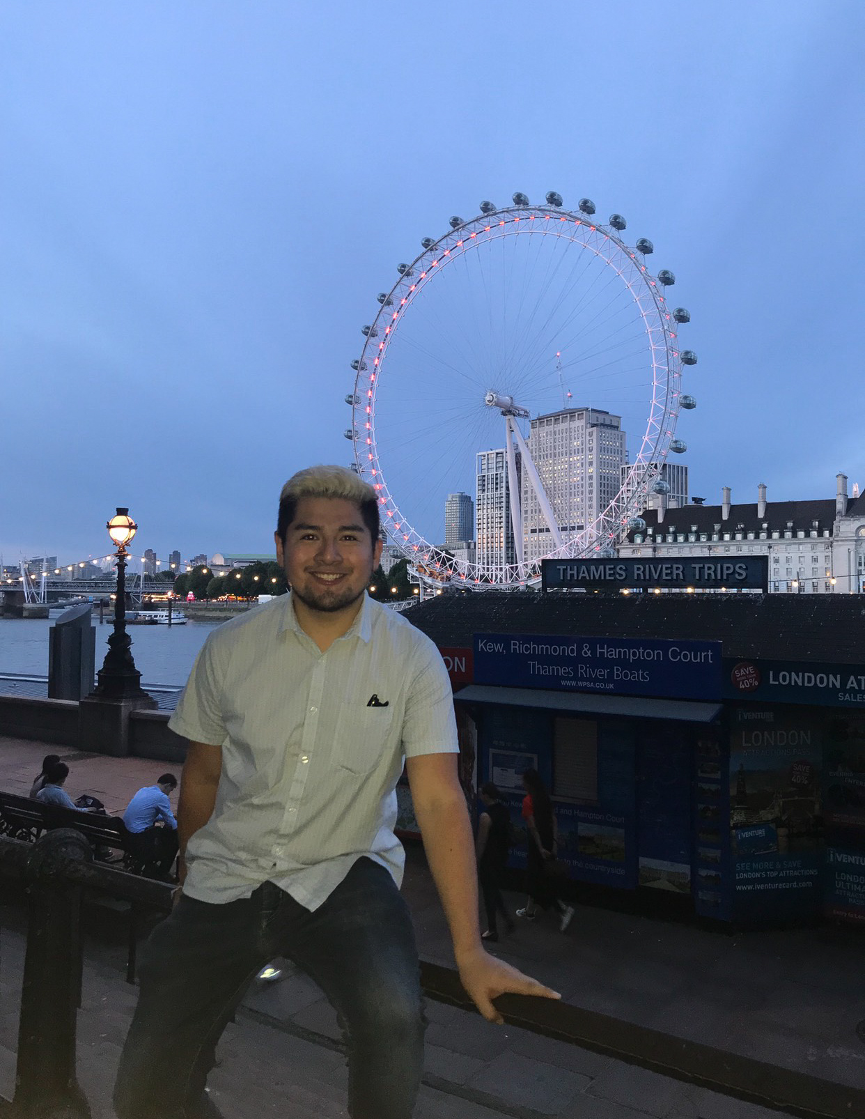 Gonzales sits on a railing at dusk, in the background is the London Eye illuminated.