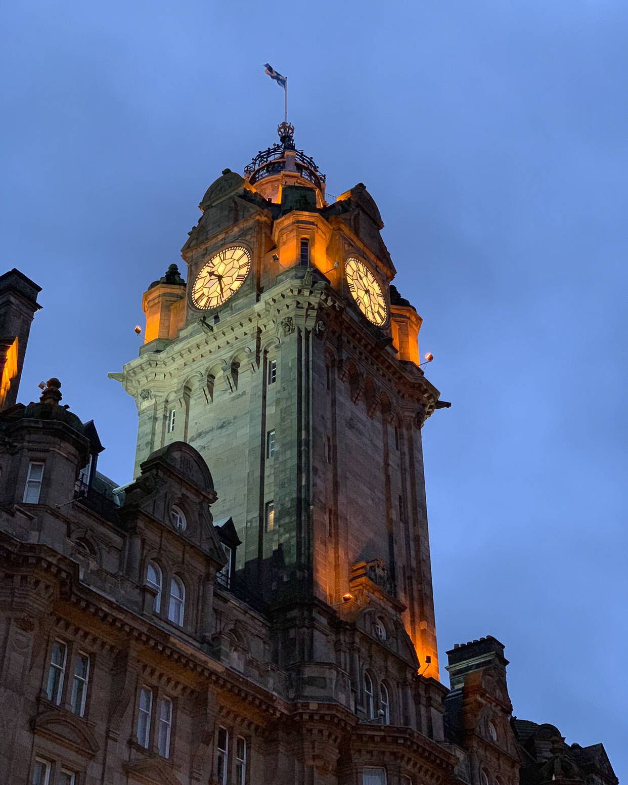 A glimpse up at an enormous stone clock tower at dusk.