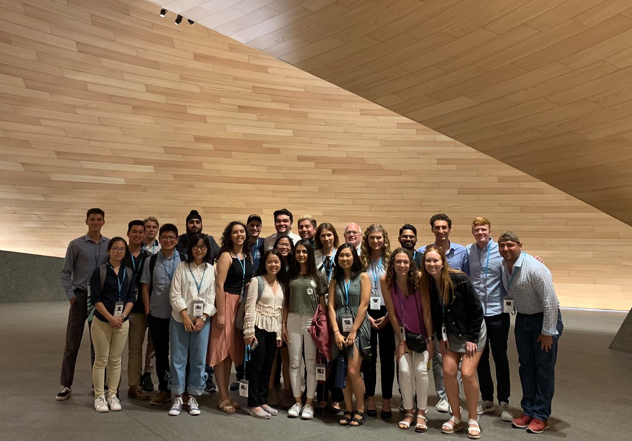 The class stands in the lobby of the Bloomberg European headquarters, an impressively tall wall of wooden planks behind them.