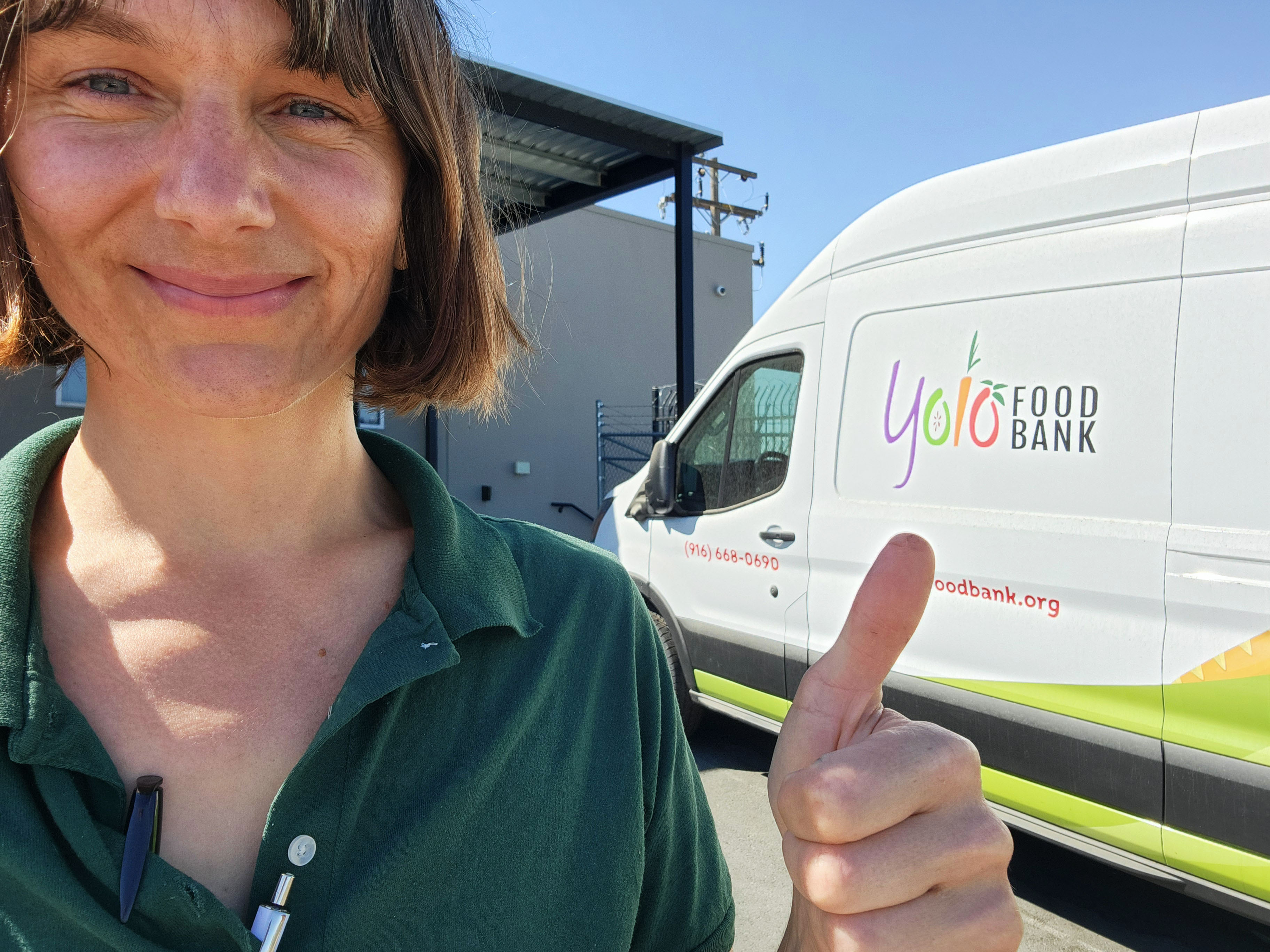Person smiling and giving a thumbs-up next to a white Yolo Food Bank van.