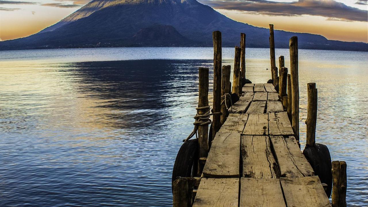 Wooden dock extending into a calm lake, with mountains and clouds in the background.