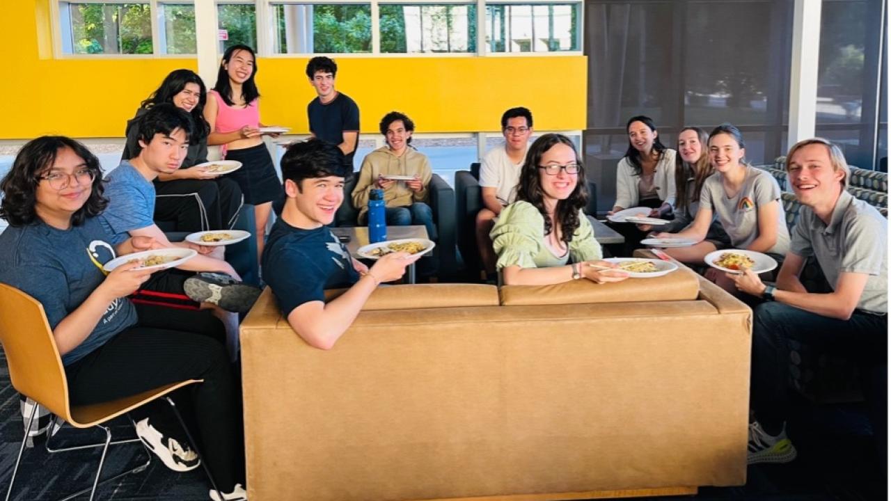 Group of students sit around a table and smile for the camera.