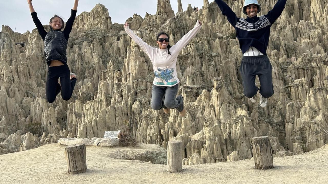 Three student in a large canyon. The all jump in the air at the same time and the photo captures them high in the air, smiling.