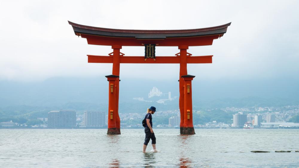 A man stands in calm water, reflecting the serene surroundings and the clear sky above.