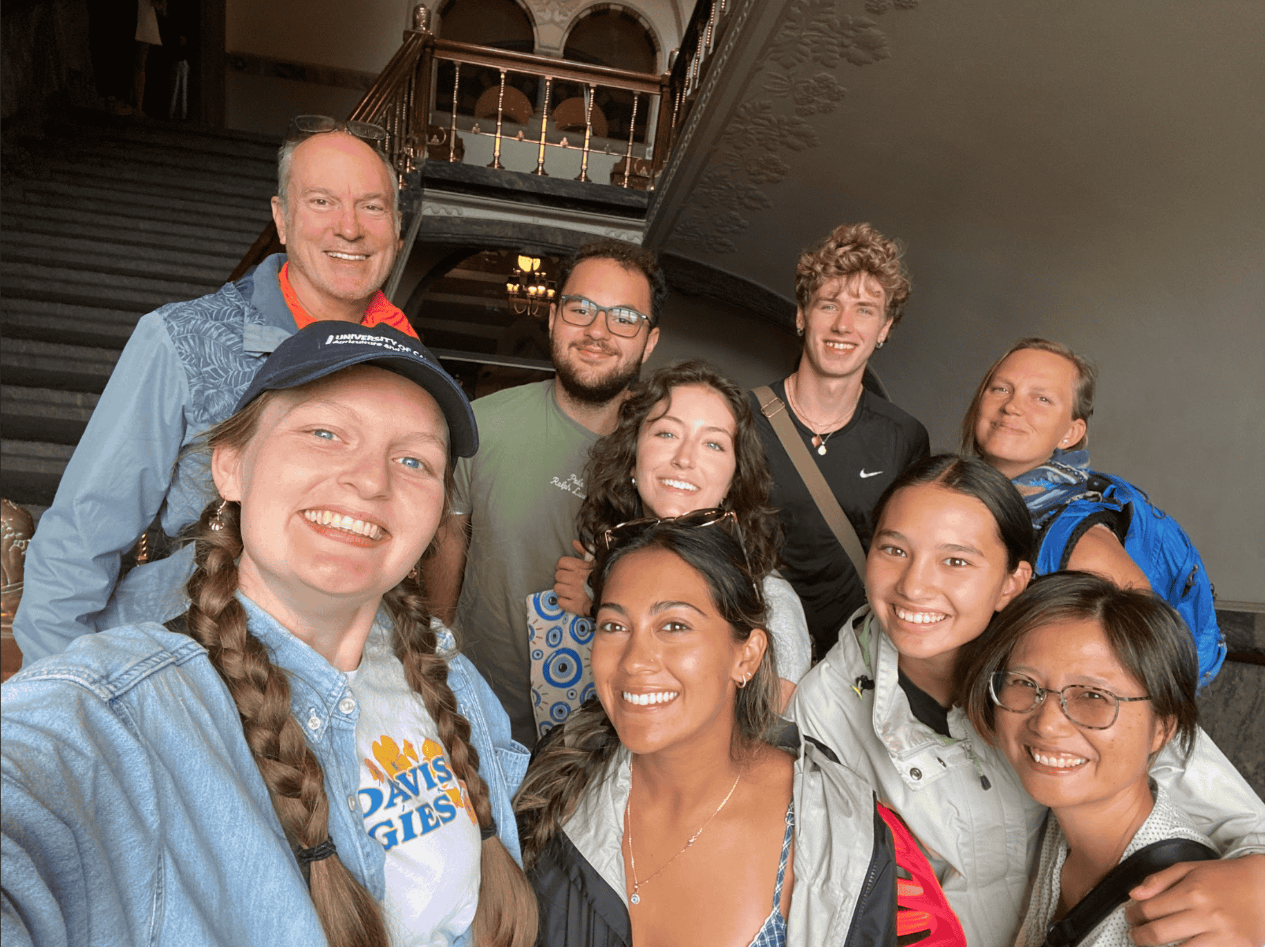 Nine smiling adults posing on an ornate indoor staircase