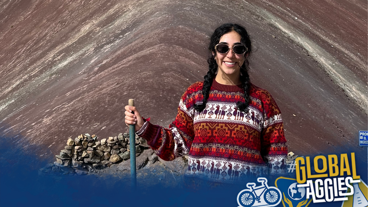 Smiling woman in colorful sweater holding hiking pole by banded red rock; small logo
