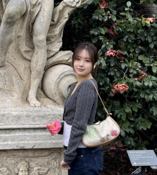 Young woman in dark sweater by stone sculpture and camellia bush, holding pink flower