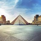 Louvre glass pyramid in courtyard with historic wings and sunrise sky