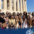 Students posing in front of ancient Greek temple columns on a sunny day, Global Aggies logo