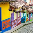 Colorful houses with ornate designs and hanging flowers line a cobblestone street.