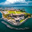 Aerial photo of coastal fortress on rocky promontory with green lawns and blue sea