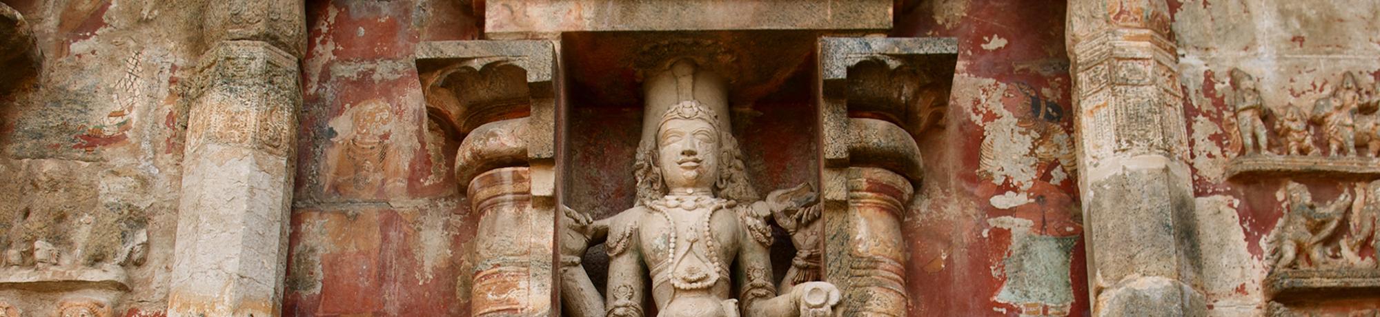Intricate stone statue of a deity set against a colorful, detailed temple wall.