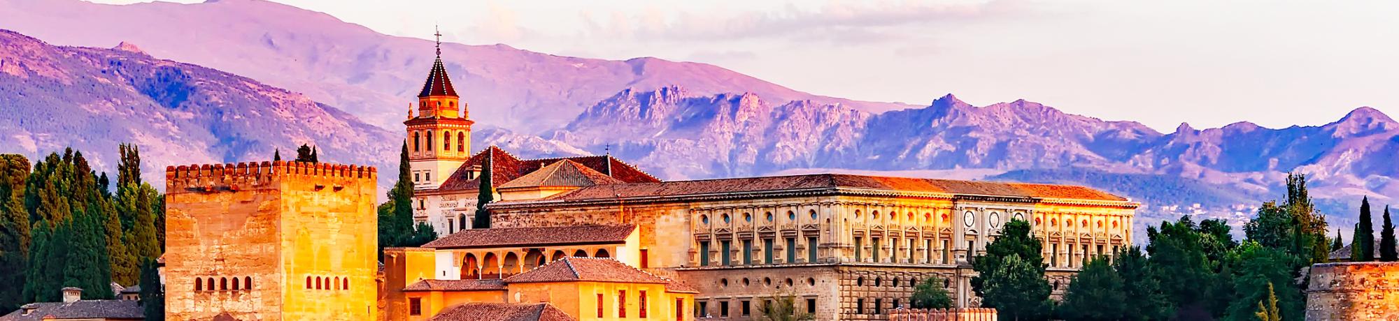 Historic building with a tower, set against a colorful mountain landscape at sunset.