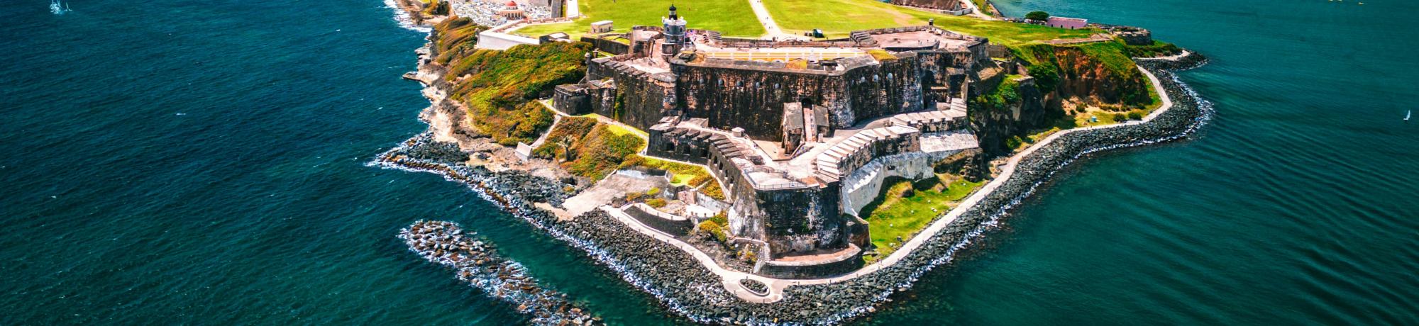 Aerial photo of coastal fortress on rocky promontory with green lawns and blue sea